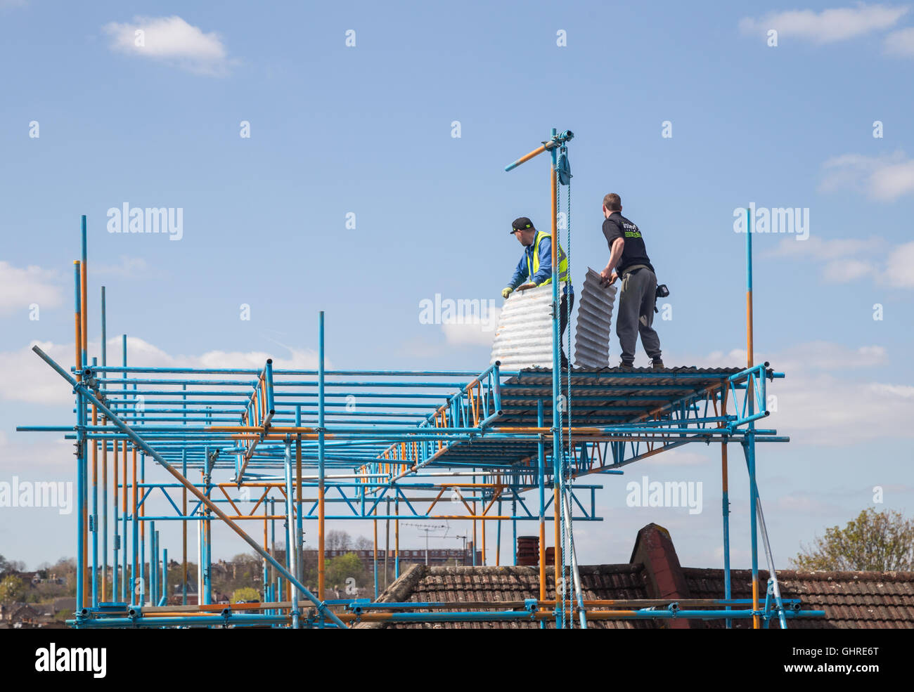 builders carrying corrugated iron sheets standing on scaffolding above