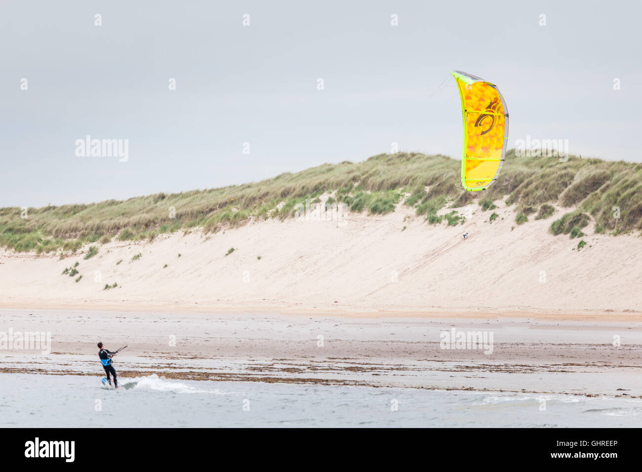 Kite surfer with a bright yellow kite and sand dunes at Beadnell Bay and beach, Northumberland Stock Photo