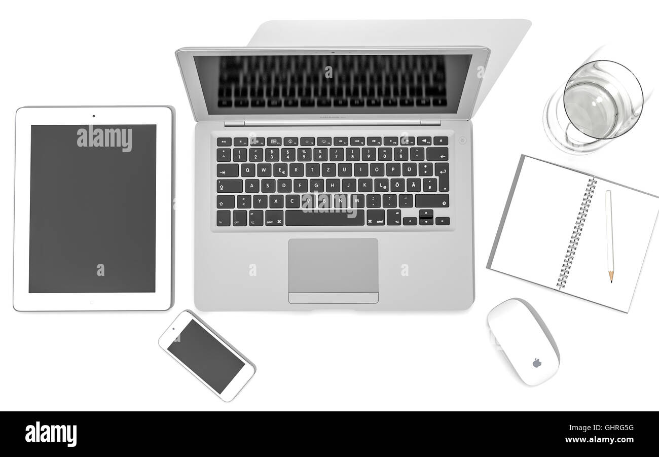 iPad, iPhone 5, Macbook Air and Apple magic mouse on a desk with a glass of water and a note book and pencil Stock Photo