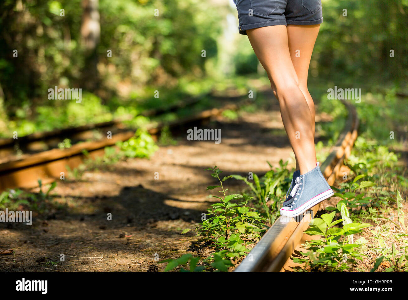 Young woman with beautiful sporty legs walking on rails in jeans sneakers Stock Photo