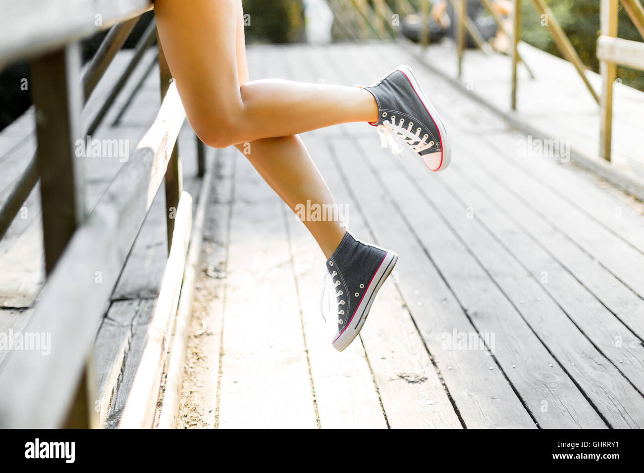 Young woman with beautiful sporty legs leaning on a wooden bridge railing in jeans sneakers Stock Photo