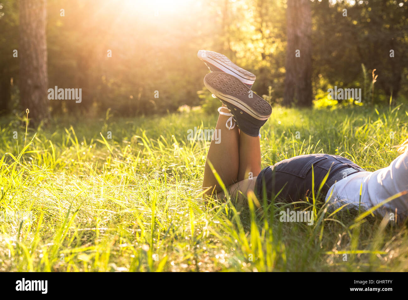 Woman legs wearing jeans sneakers lying on a grass in a forest lawn in the evening Stock Photo