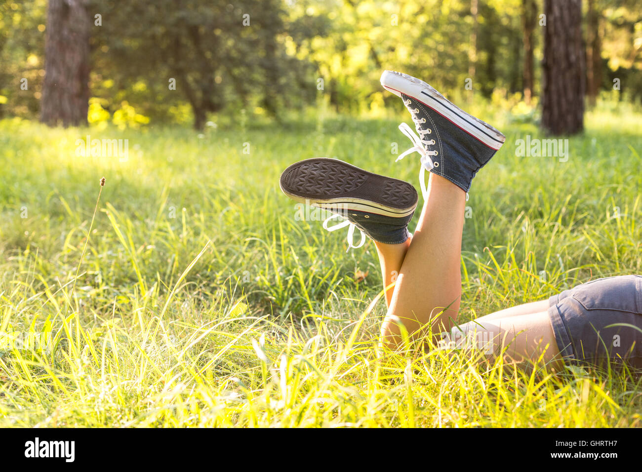 Woman legs wearing jeans sneakers lying on a grass in a forest lawn in the evening Stock Photo