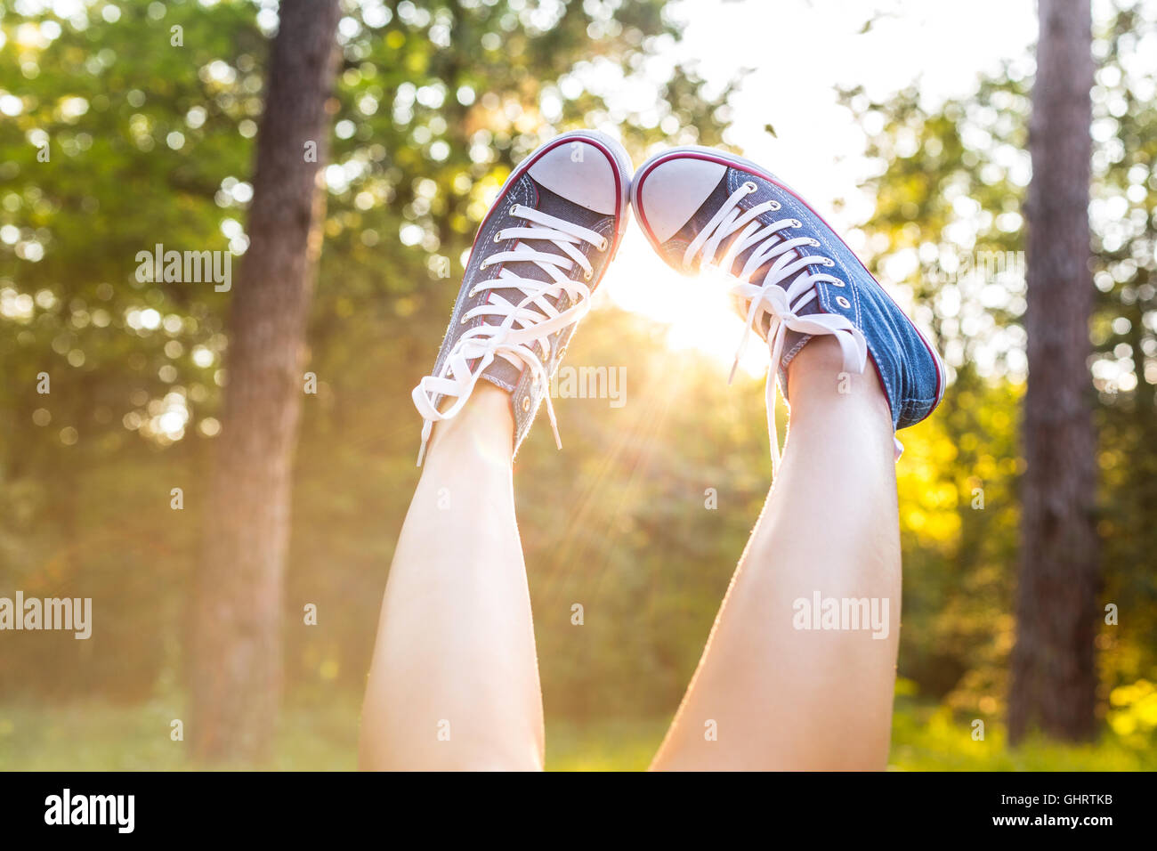 Close view of woman legs  wearing jeans sneakers over a sunset rays in a forest Stock Photo