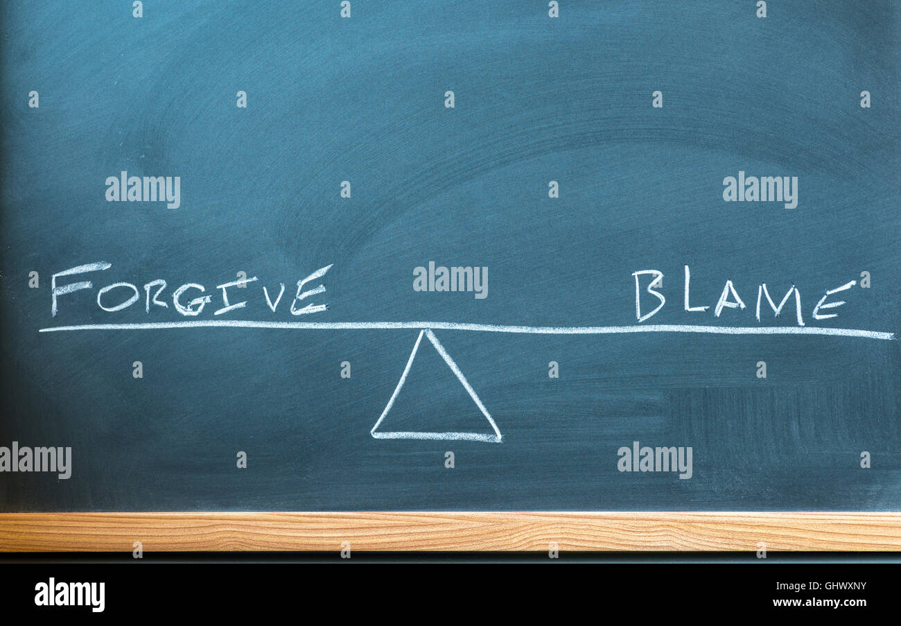 the words forgive and blame on a scale in equilibrium written on a chalkboard. Stock Photo