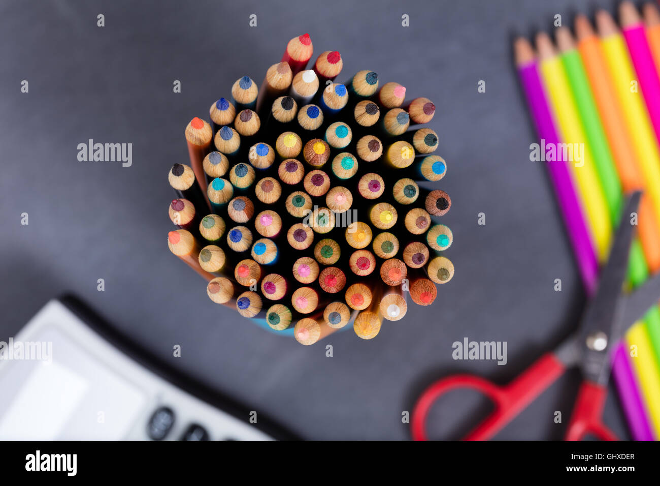 Selective focus on close up top view of colorful pencil tips with school supplies and erased chalkboard in background. Stock Photo