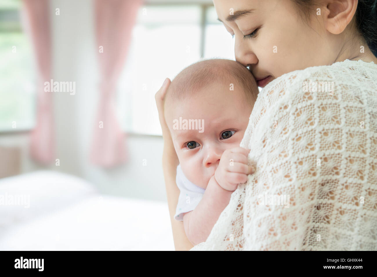 Picture of happy Asian mother kiss infant baby boy after cry. Closeup at mother and infant baby. Stock Photo