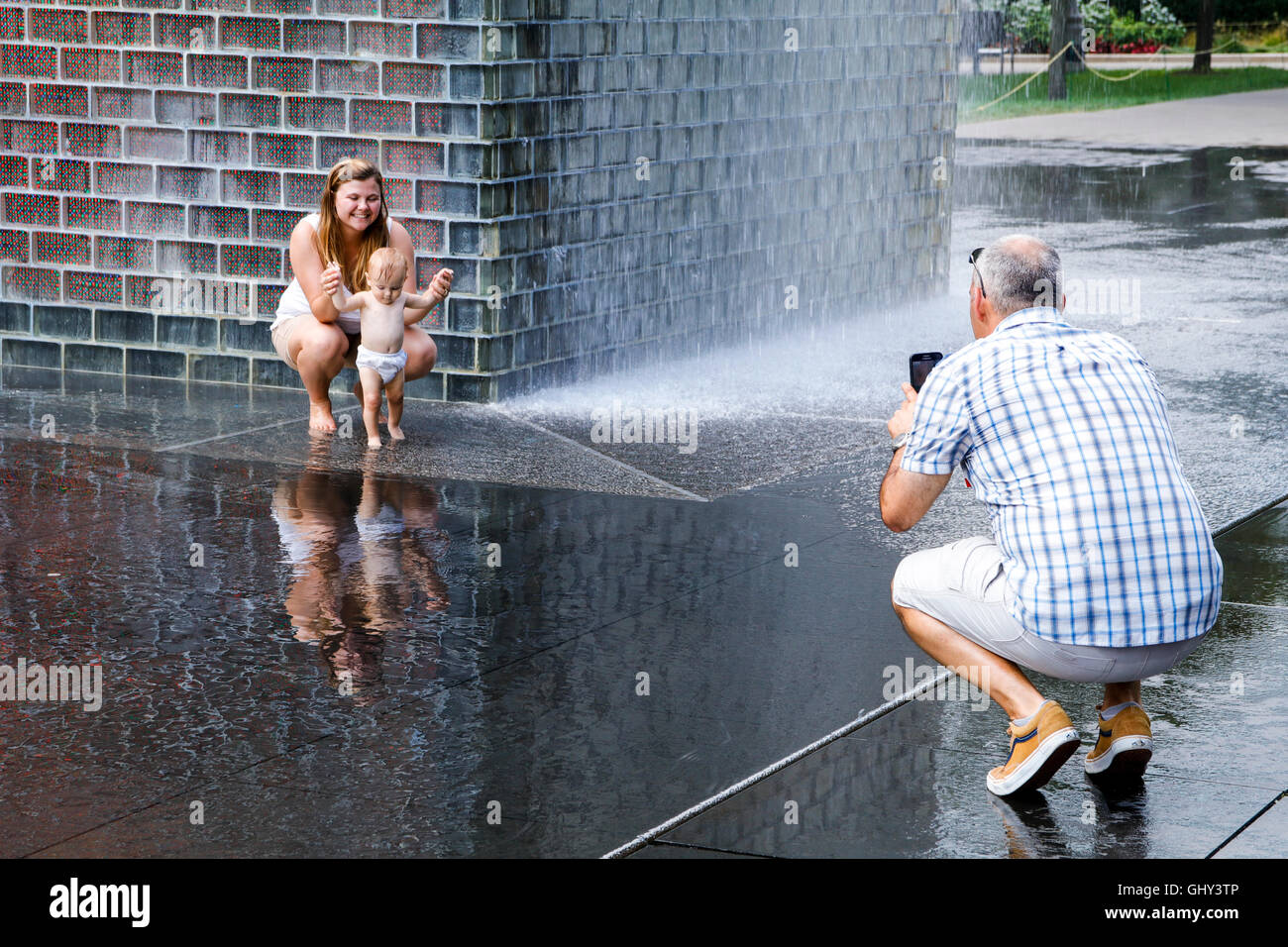 Father taking cell phone photo of mother and baby. Crown Fountain, Chicago, Illinois. Stock Photo