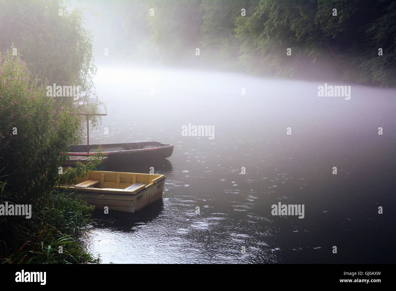 Fishing boats on river anchoring near the shore in fog. Fog is over the river. Stock Photo