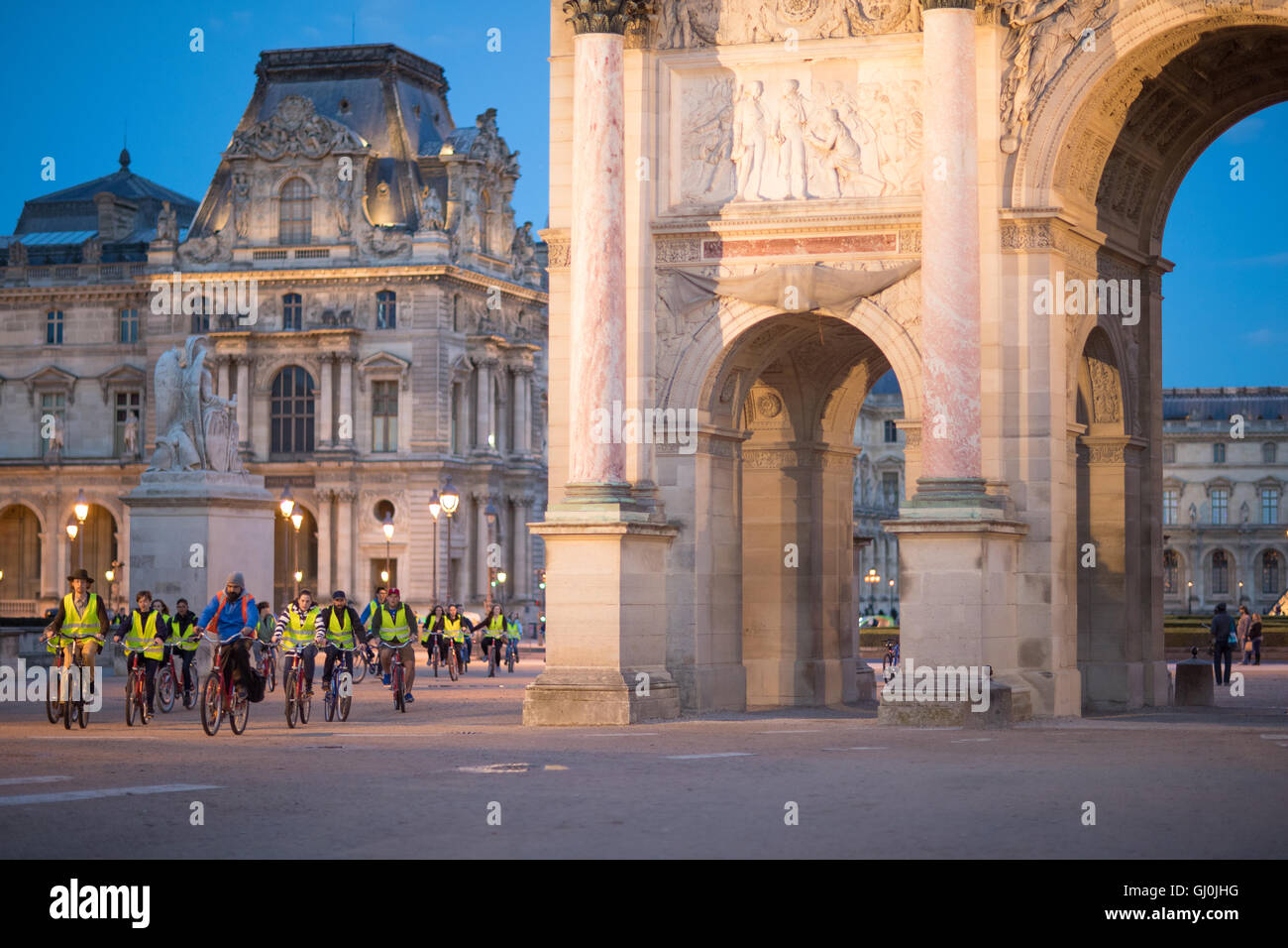 a tour by bike group pass the Arc de Triomphe du Carrousel & Palais du Louvre at dusk, Paris, France Stock Photo