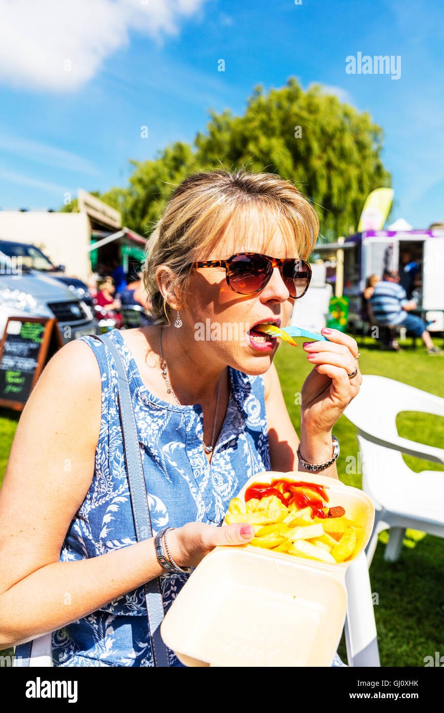 Eating chips from tray outside lady eat chips ketchup takeaway food chip shop plastic fork UK England GB Stock Photo