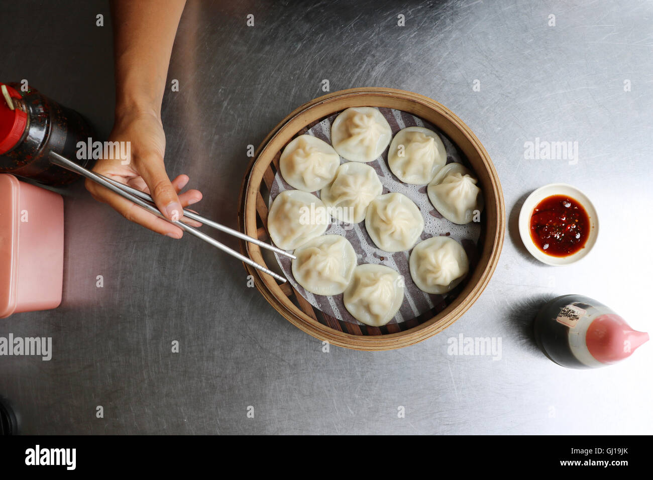 Womens hand grabbing traditional fresh chinese dumplings in wooden box on metal table with chopsticks. Stock Photo