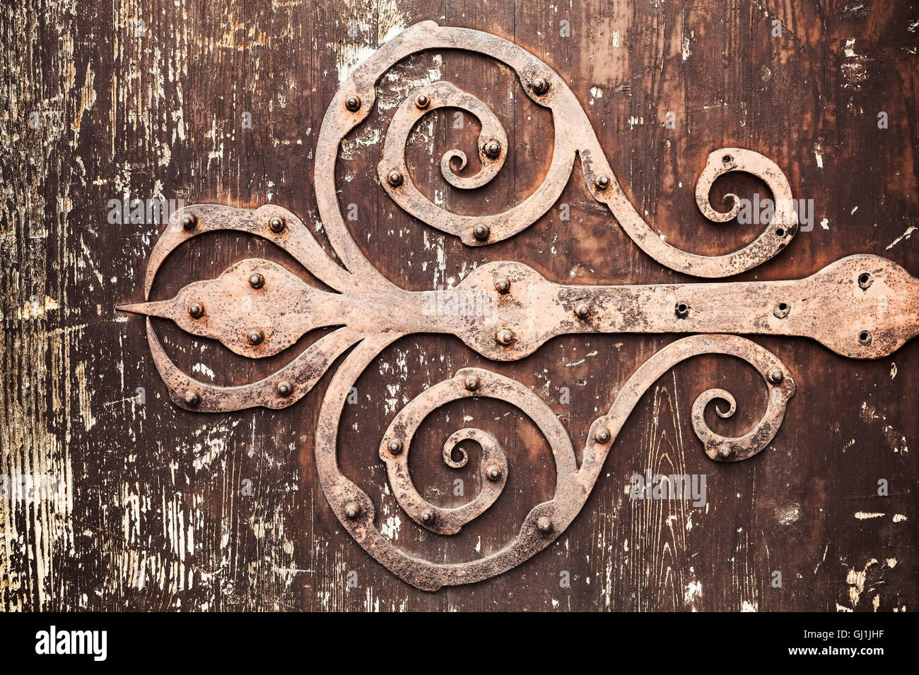 Old rusted forged decorative door hinge on vintage wooden board, closeup photo texture with retro tonal correction photo filter Stock Photo