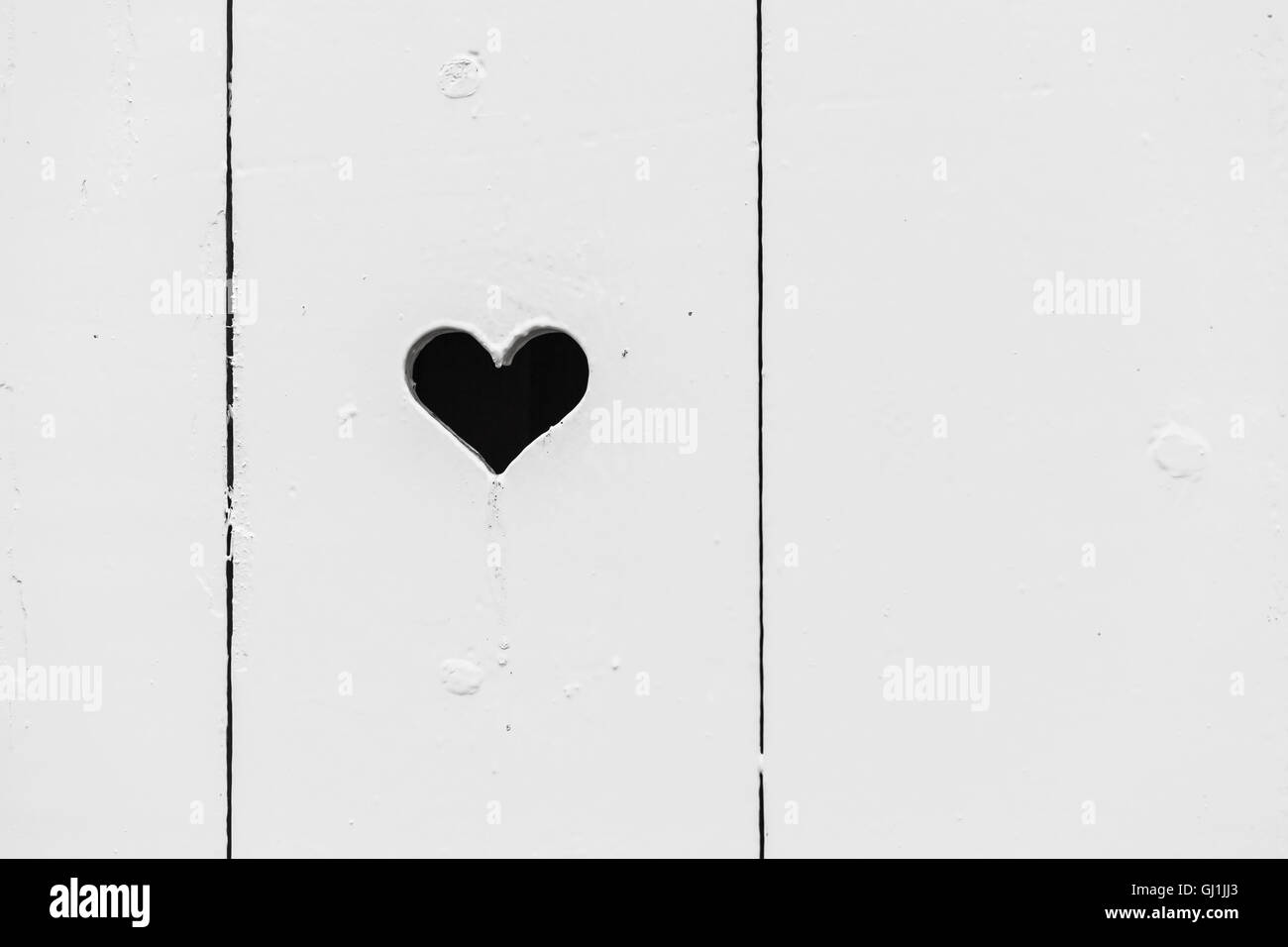 Black heart shaped hole in white wooden wall, background photo texture Stock Photo