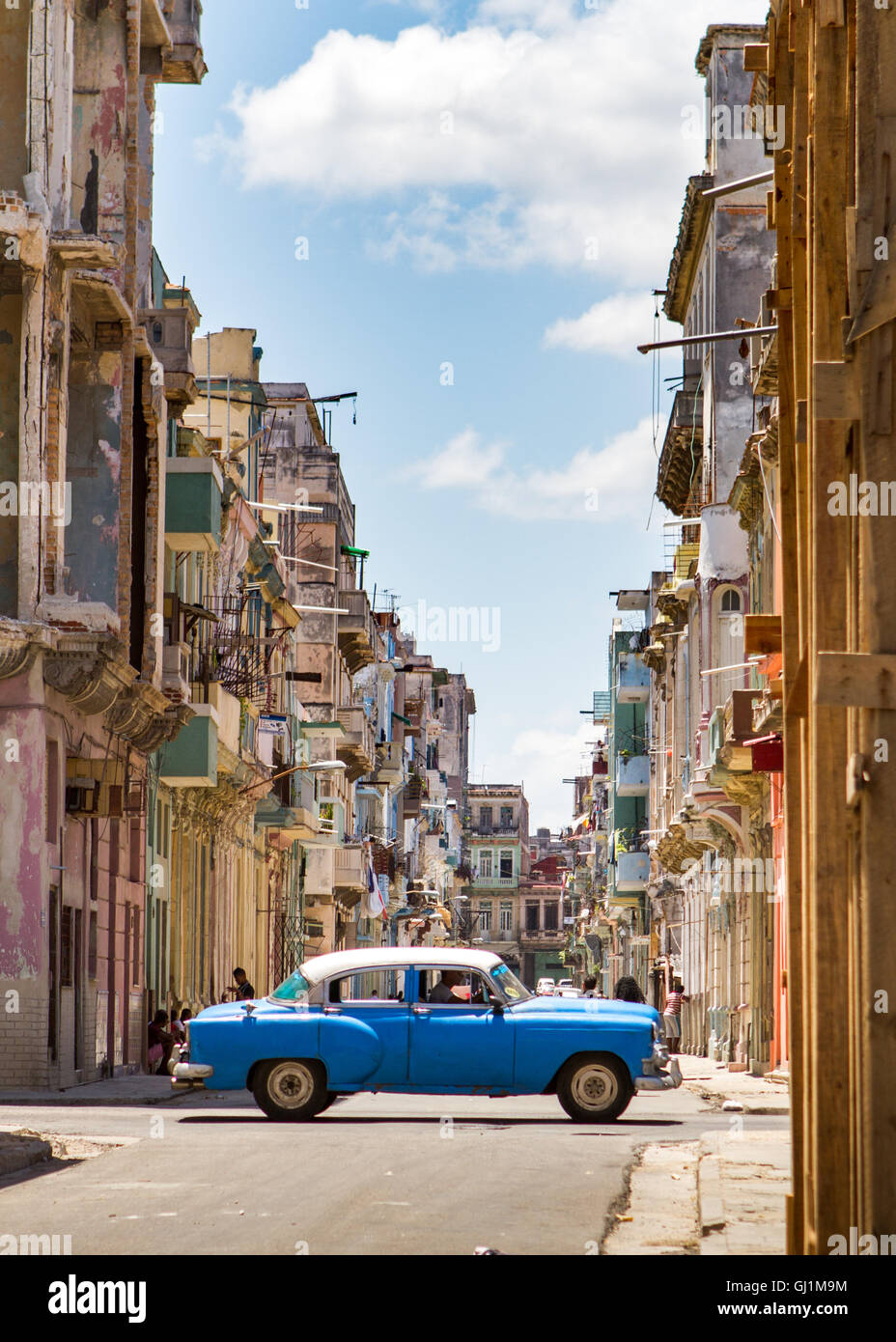 vintage blue car driving on a cross street, in typical colonial, dilapidated street on a sunny day, Havana, Cuba, 2013 Stock Photo