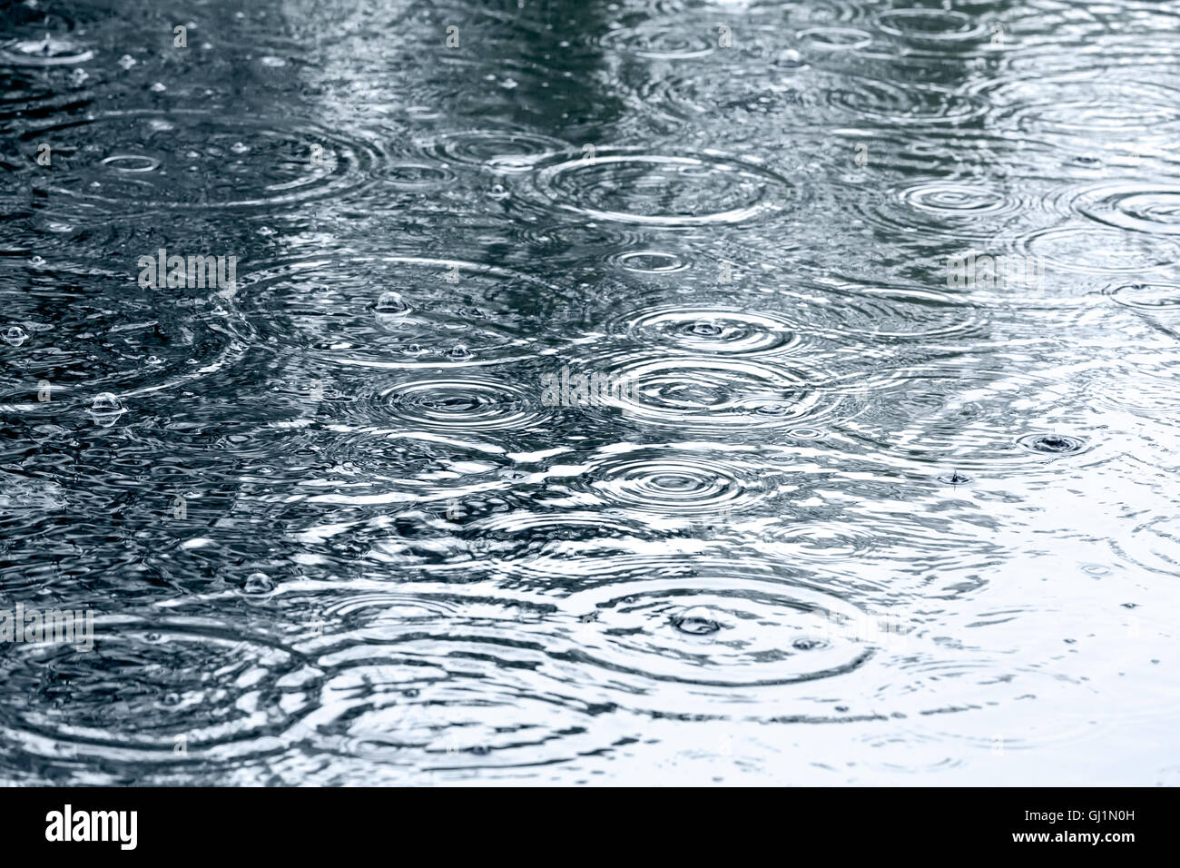 sidewalk with rain drops and ripples in puddles Stock Photo