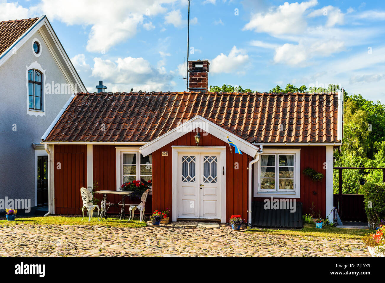 Pataholm, Sweden - August 9, 2016: Small red wooden house by the village square in the evening. Outdoor furniture in front of bu Stock Photo