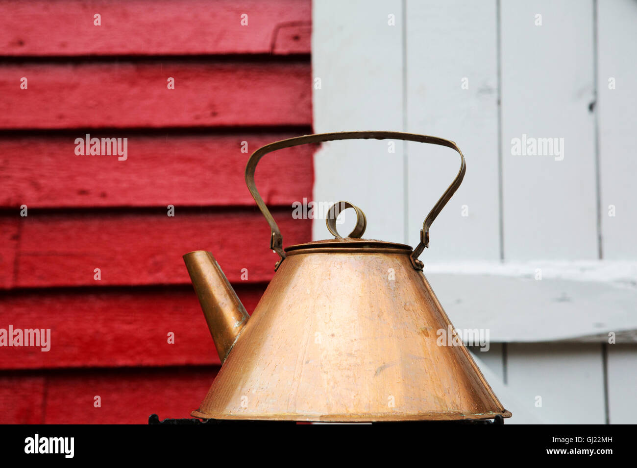 A copper kettle outside of a  red store with a white door at Bay Roberts in Newfoundland and Labrador, Canada. Stock Photo