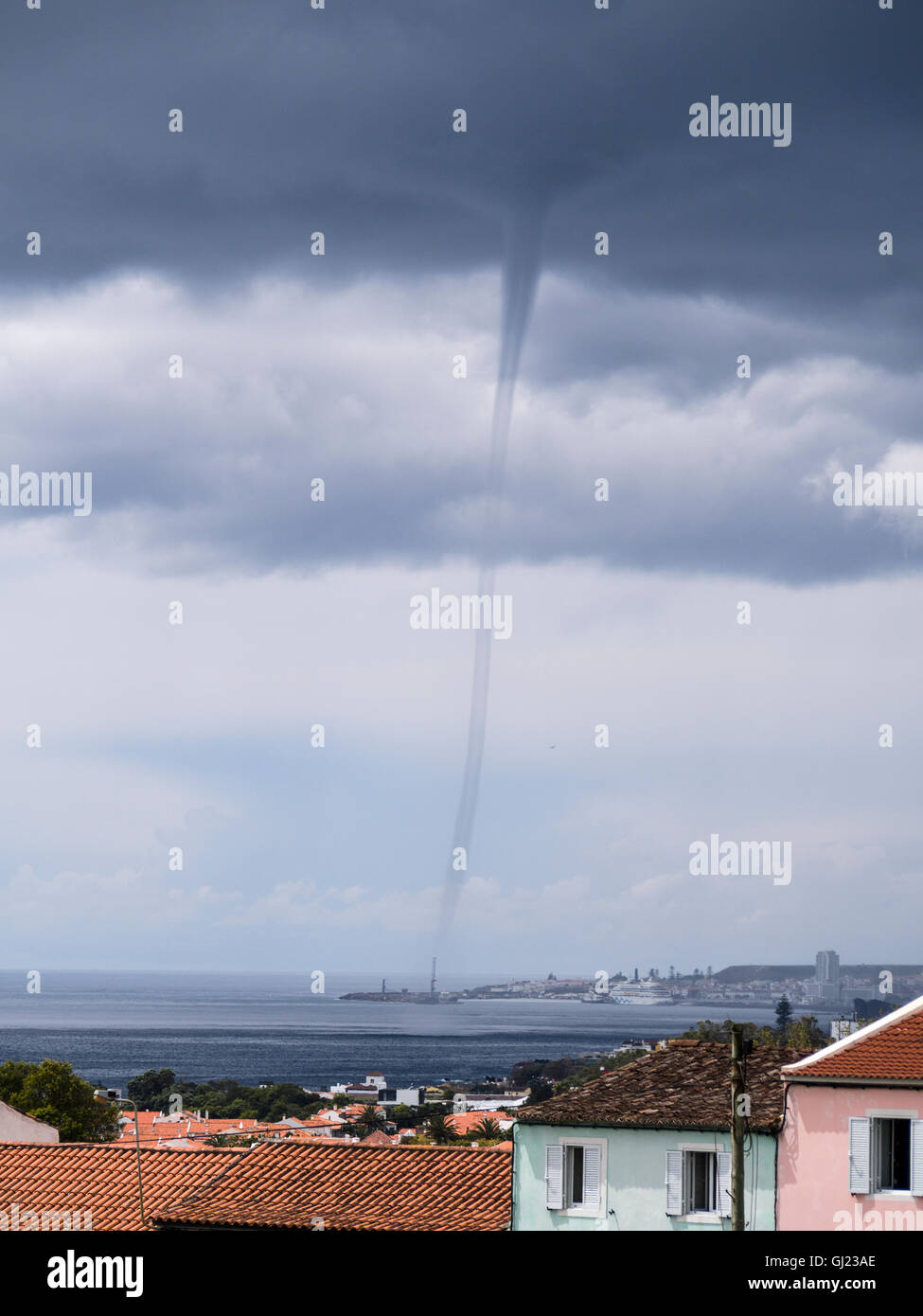 Waterspout over Ponta Delgada. A tornadic waterspout appears from the dark storm clouds in the ocean just beyond the city centre Stock Photo
