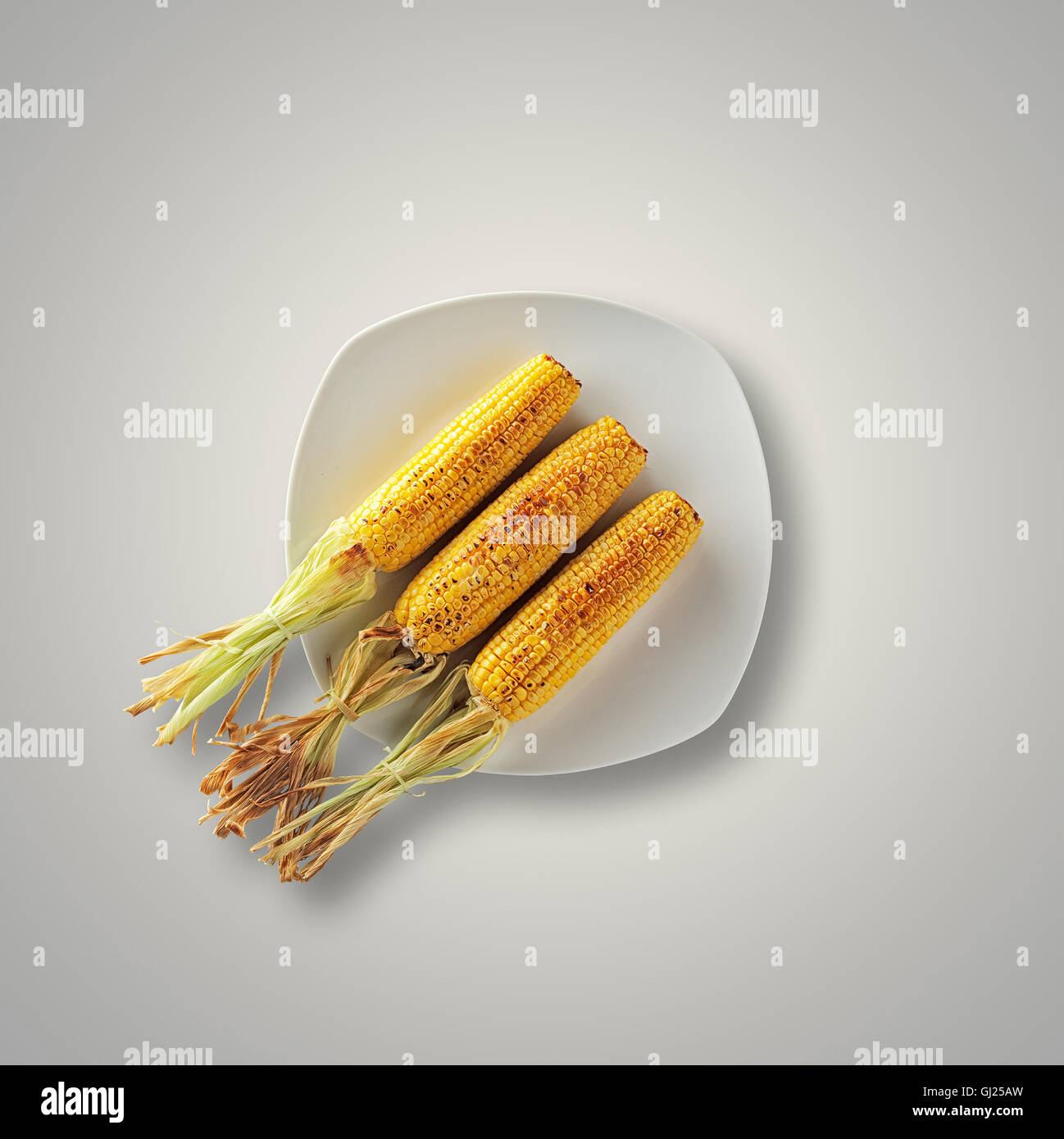 Whole Grilled Sweet Corn on a white plate and table from above Stock Photo