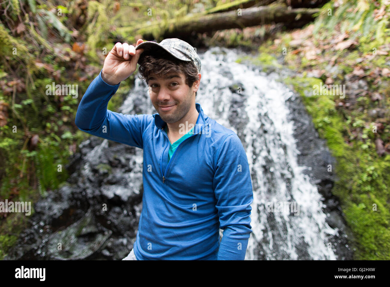 Man in front of waterfall wearing baseball cap looking at camera smiling Stock Photo