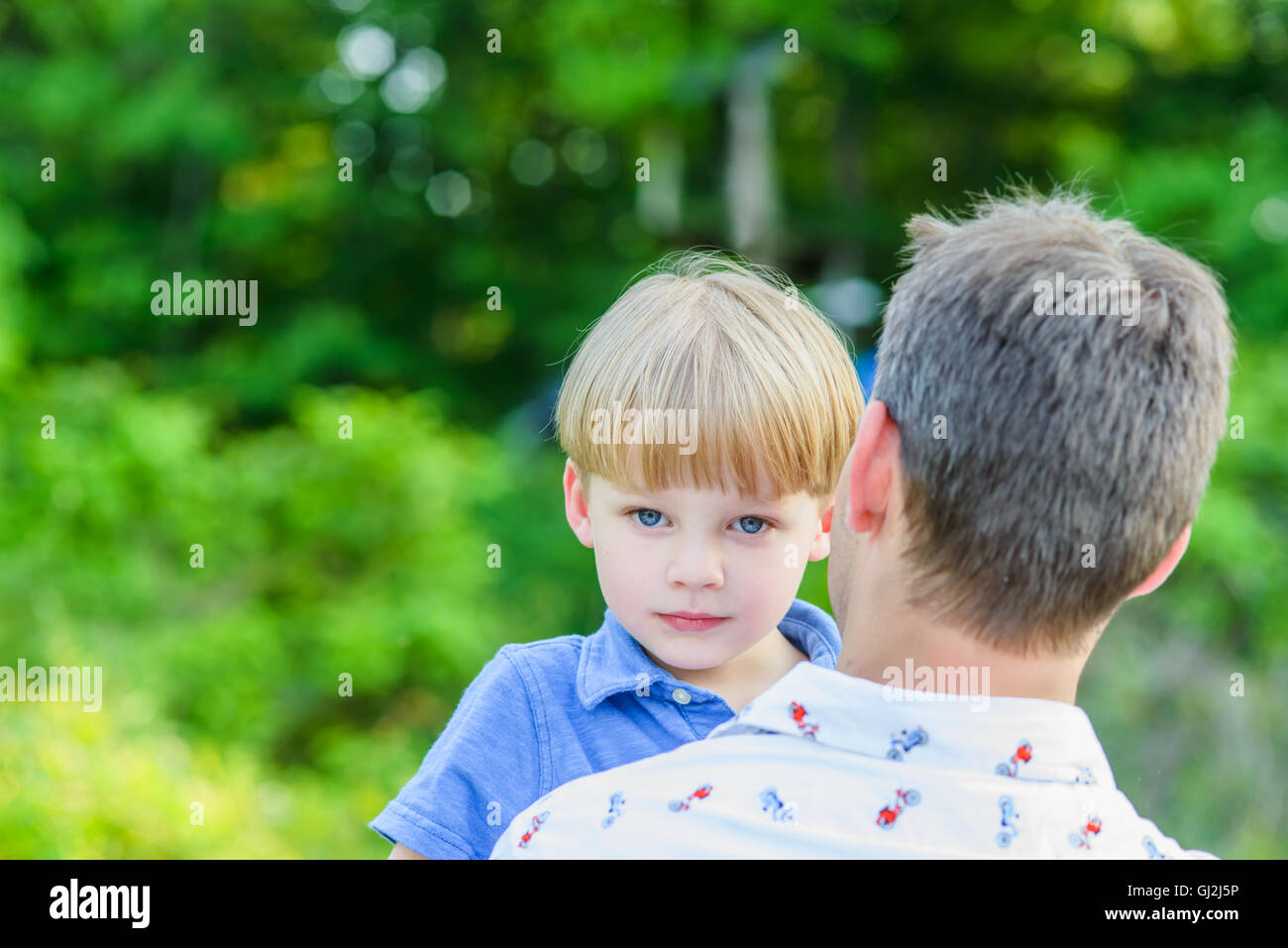 Boy looking at camera over fathers shoulders Stock Photo