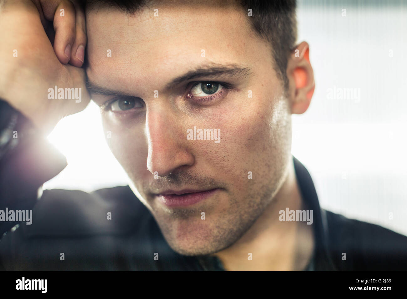 Close up portrait of young man, hand on head, looking at camera Stock Photo