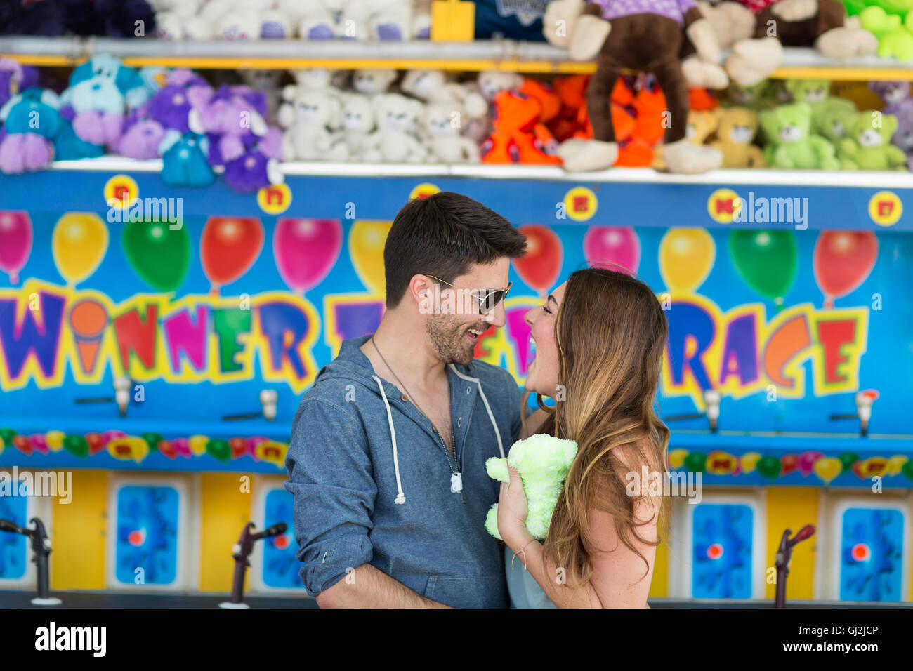 Couple in front of fairground shooting gallery face to face smiling, Coney island, Brooklyn, New York, USA Stock Photo