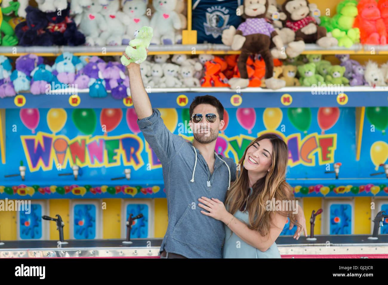 Couple in front of fairground shooting gallery holding teddy bear, Coney island, Brooklyn, New York, USA Stock Photo
