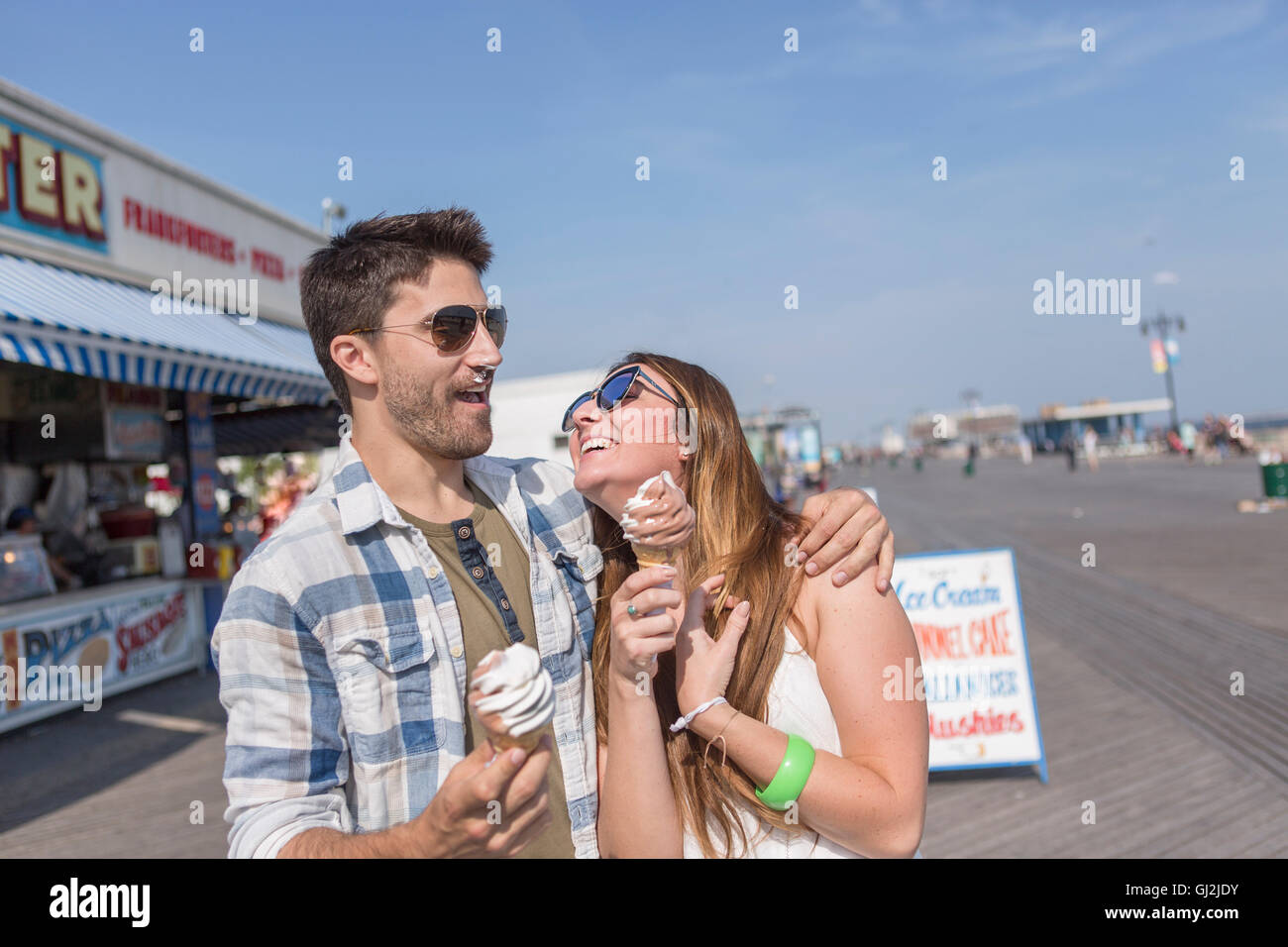 Couple on promenade holding ice cream cones smiling, Coney island