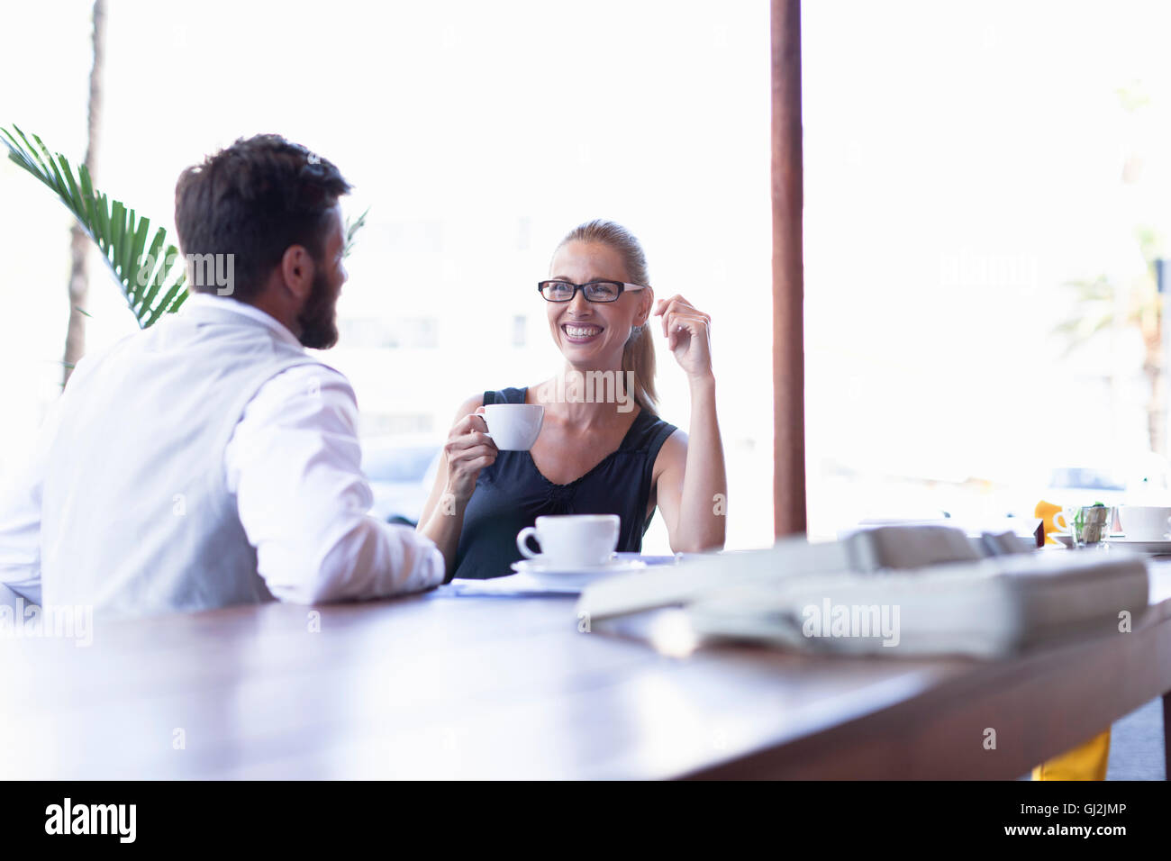 Mature man and woman, sitting outside cafe, drinking coffee, face to face, smiling Stock Photo