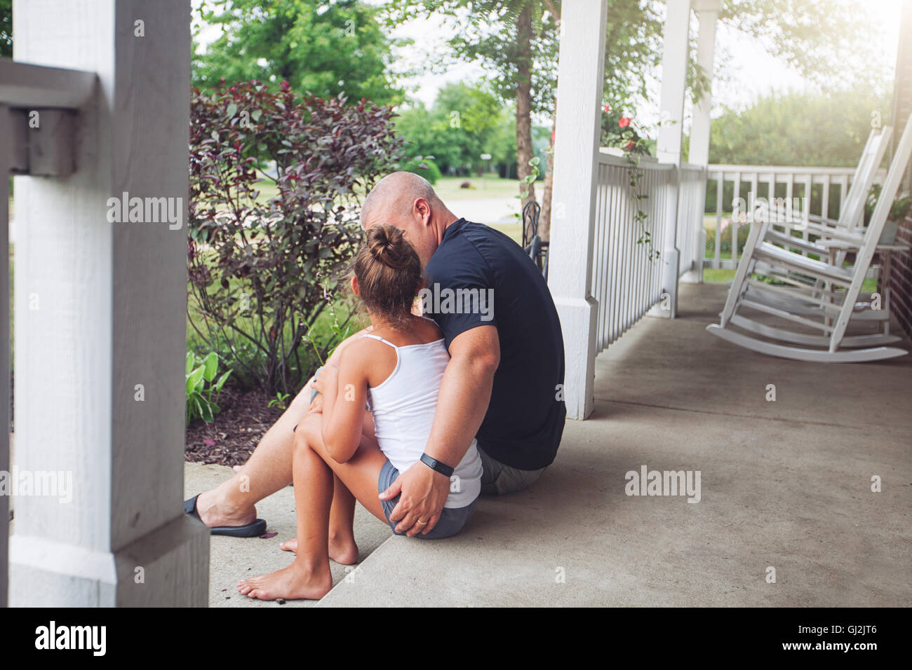 Rear view of father sitting on porch with arm around daughter Stock Photo