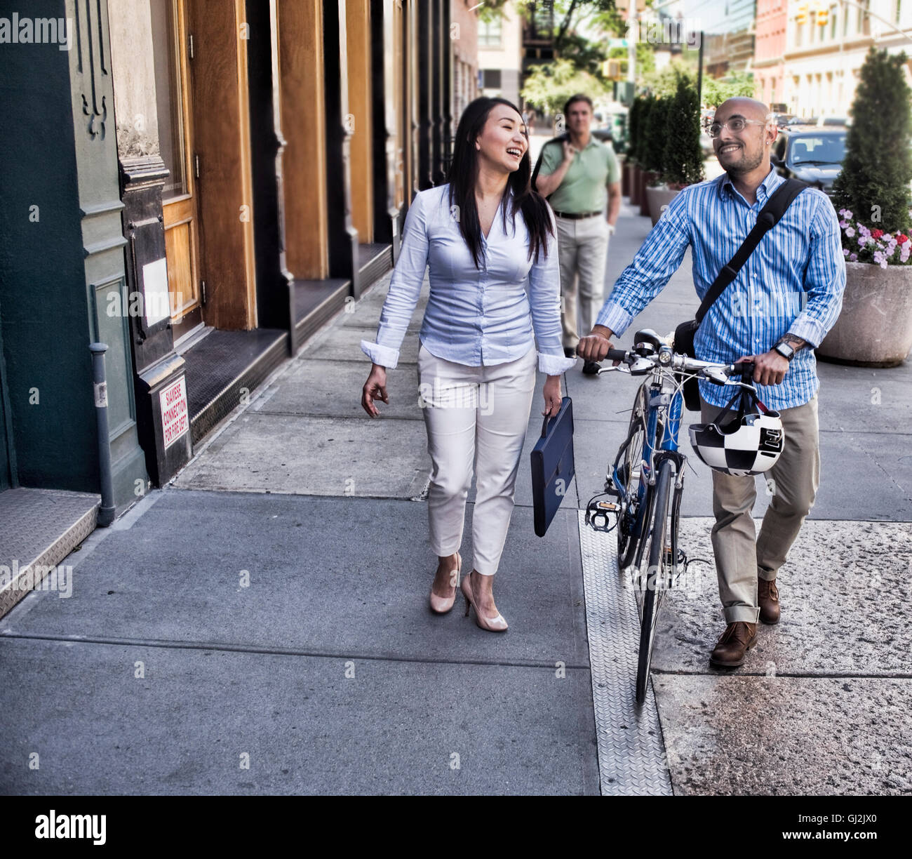 Business man and woman walking in street, man pushing bike, smiling Stock Photo
