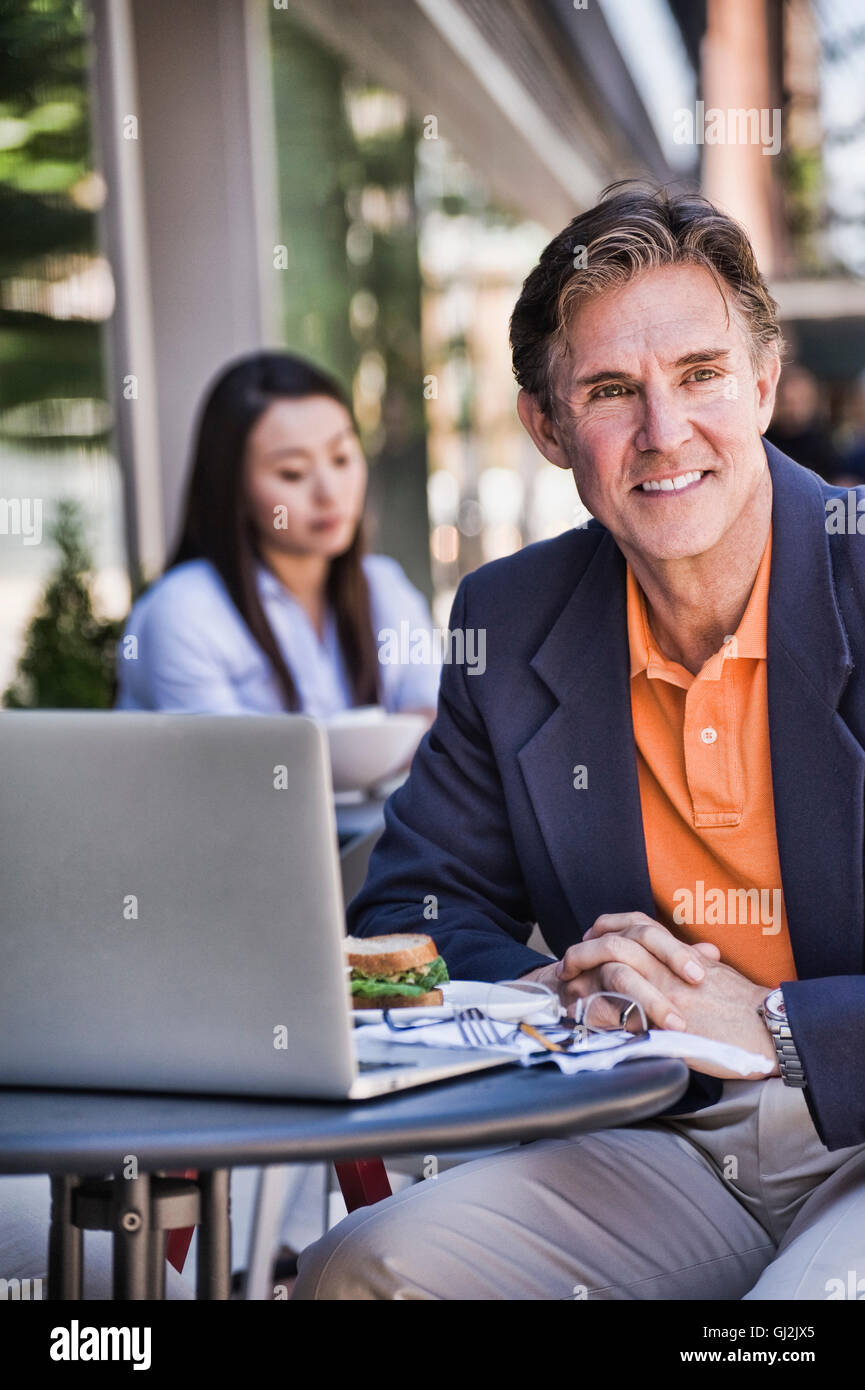 Businessman sitting outside cafe, using laptop Stock Photo - Alamy