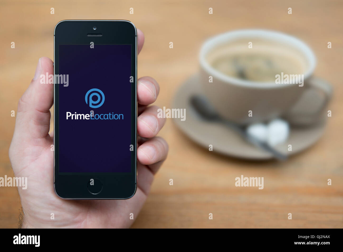 A man looks at his iPhone which displays the Prime Location logo, while sat with a cup of coffee (Editorial use only). Stock Photo