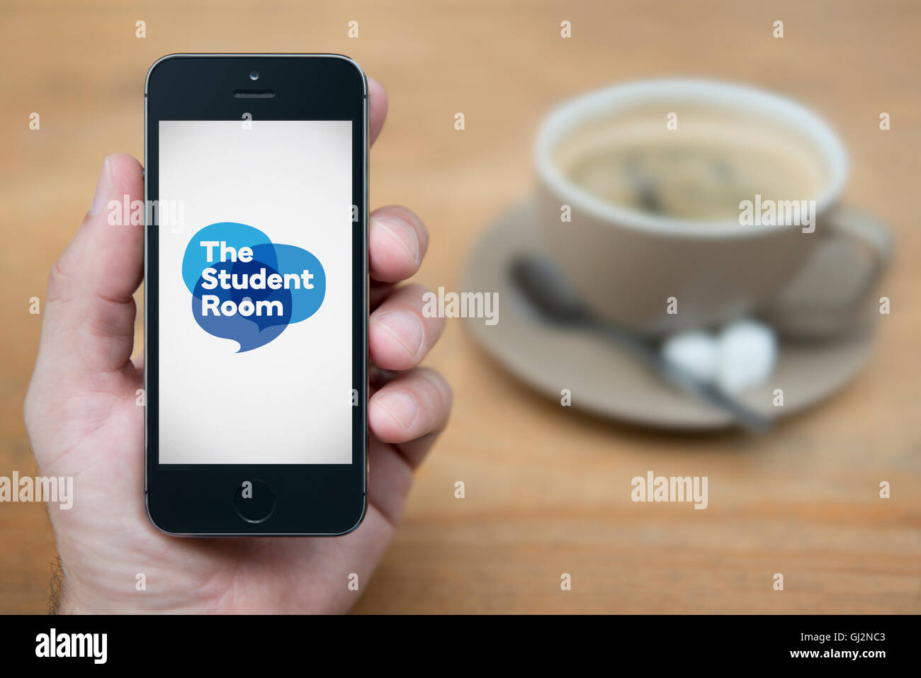 A man looks at his iPhone which displays the Student Room logo, while sat with a cup of coffee (Editorial use only). Stock Photo