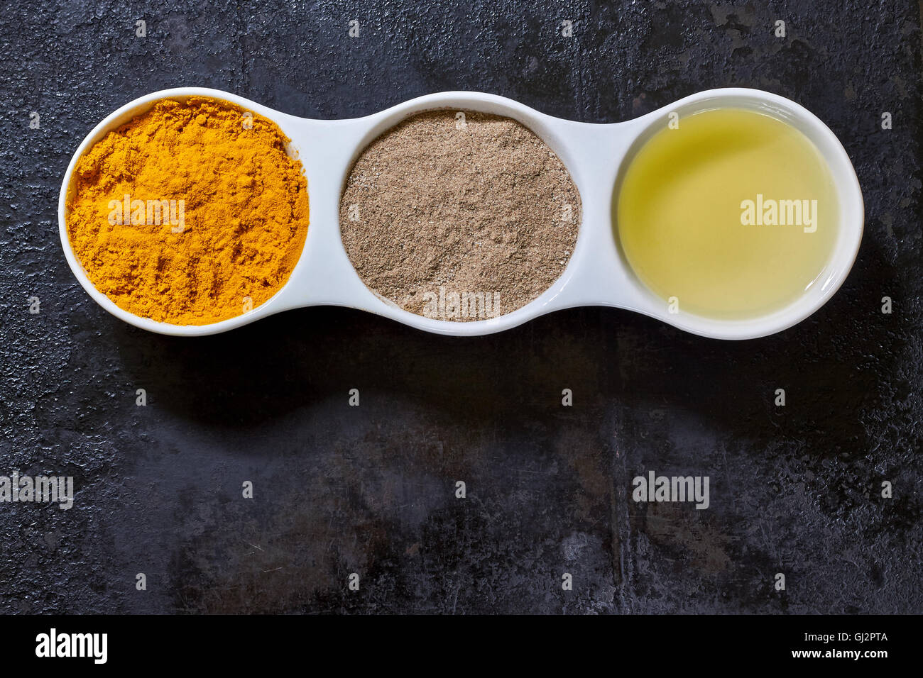 Turmeric, black pepper and olive oil in white ceramic bowl on black rustic background