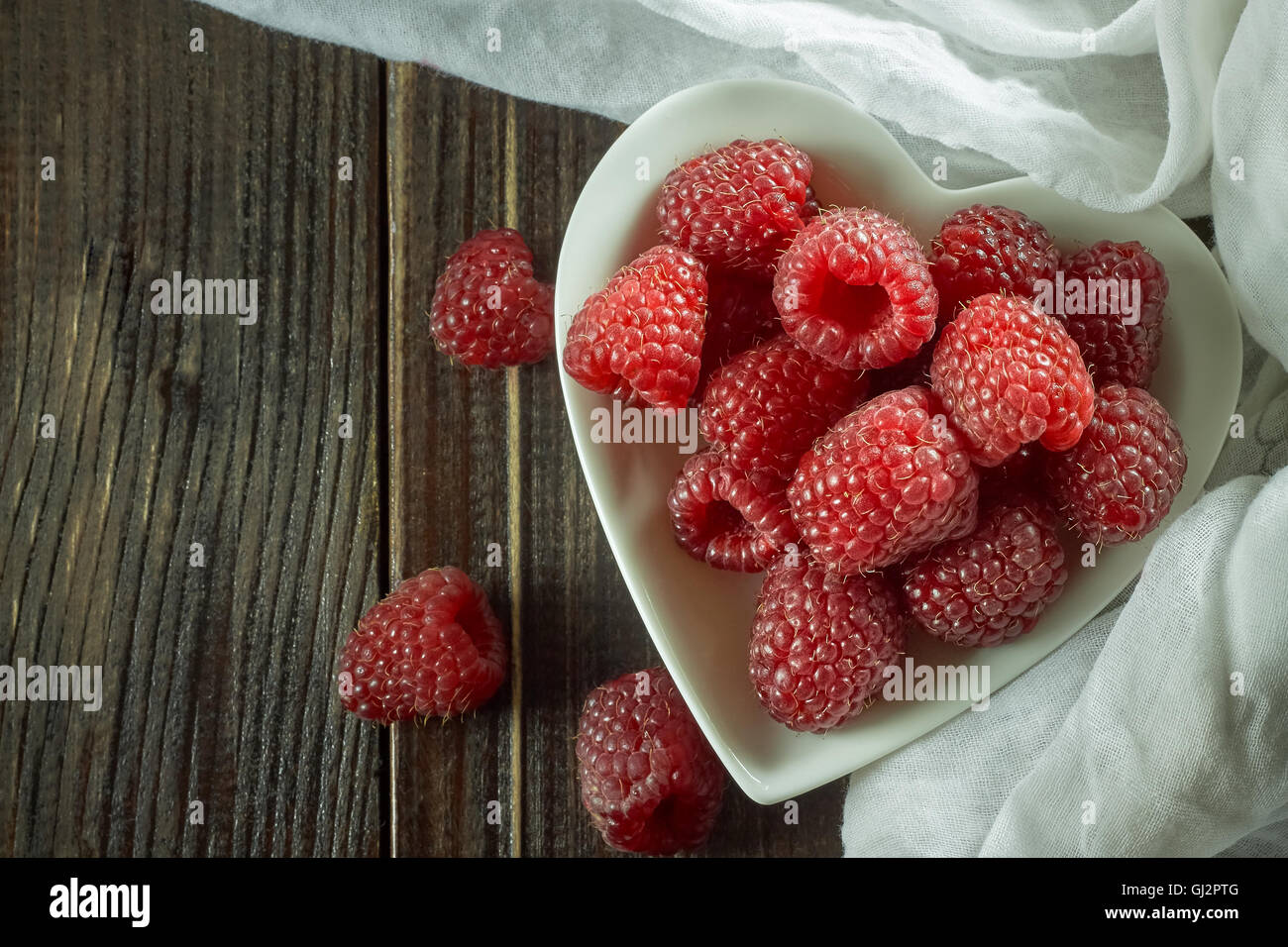 Red raspberries in white ceramic heart shaped bowl on wooden background. Top view with copy space Stock Photo