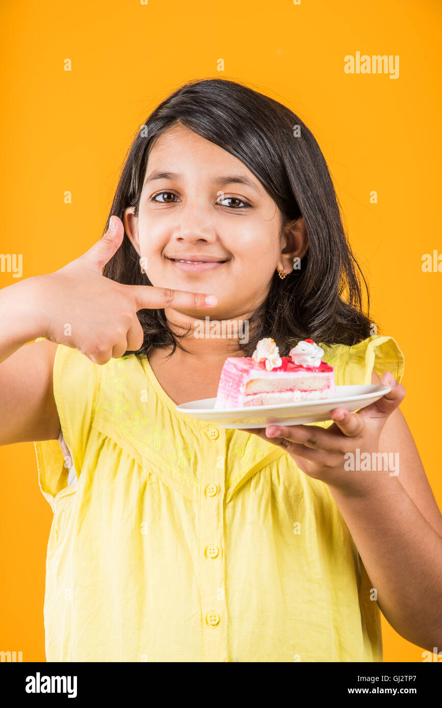 portrait of Indian kid eating cake or pastry, cute little girl eating cake, girl eating chocolate cake over colorful background Stock Photo
