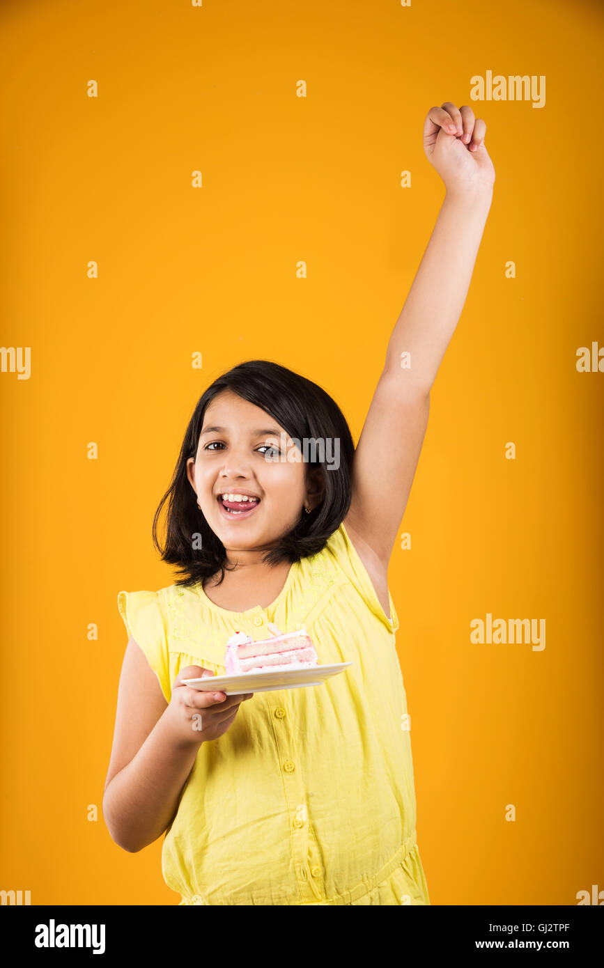 portrait of Indian kid eating cake or pastry, cute little girl eating cake, girl eating chocolate cake over colorful background Stock Photo