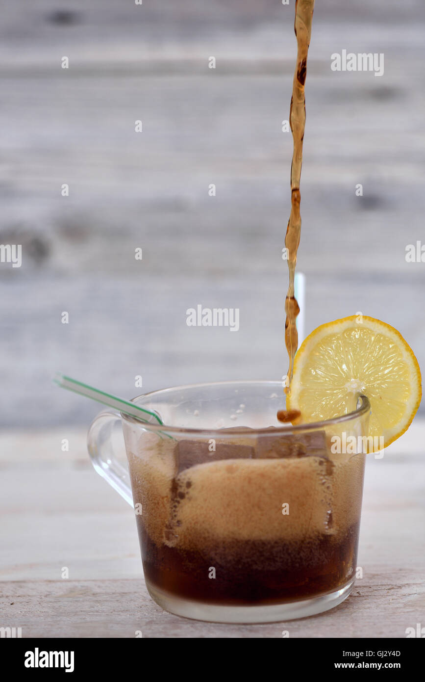 Pouring cola drink in a glass with ice cube, lemon slice and straw on ...