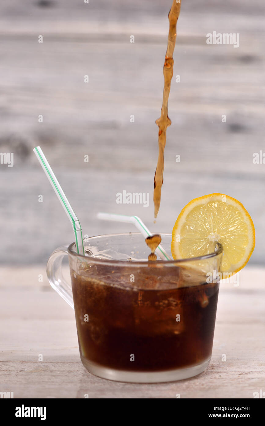 Pouring cola drink in a glass with ice cube, lemon slice and straw on ...