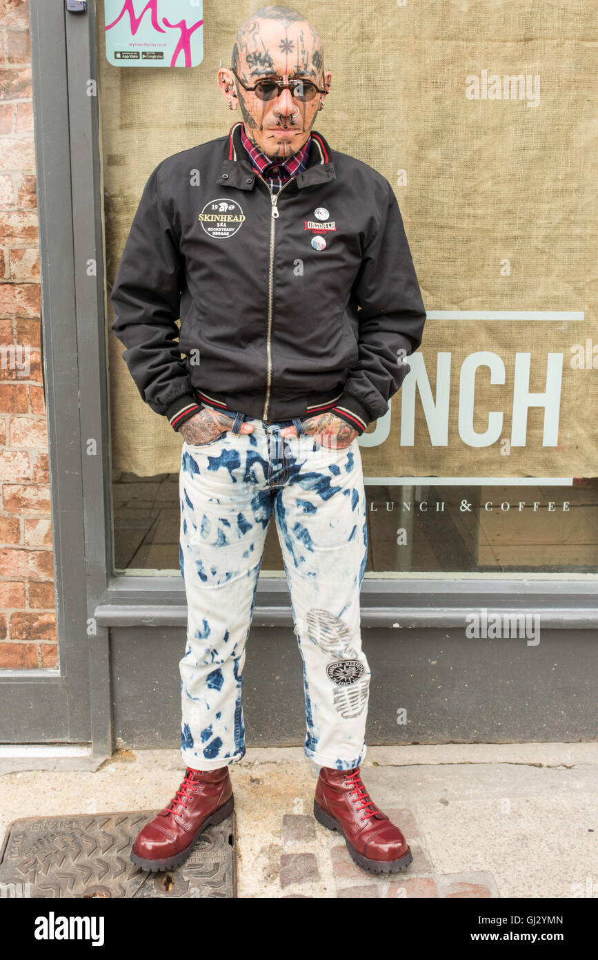 A heavily tattooed French punk, with facial piercings, in jeans and red Doc Martens standing outside a shop on the high street in Canterbury, Kent. Stock Photo