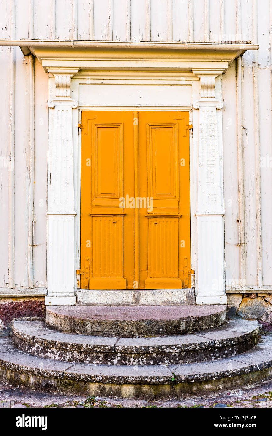 Old and weathered yellow double door without handle on a white house. Stock Photo