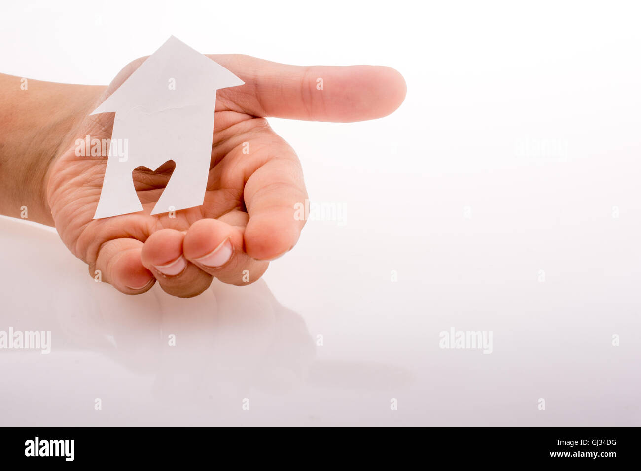 Hand holding a paper house with a heart carved in it on a white ...