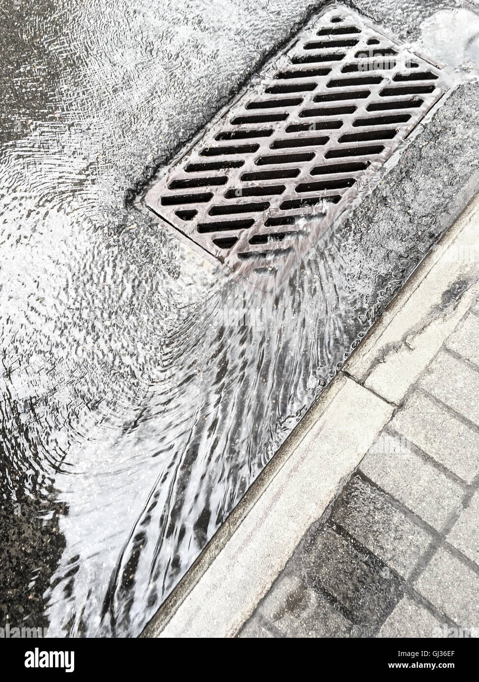 rain water flows down through sewer grate on street Stock Photo