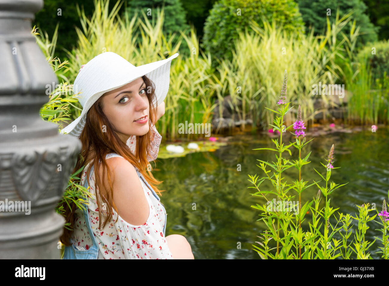 Beautiful woman in white hat sitting near the lake with various plants ...