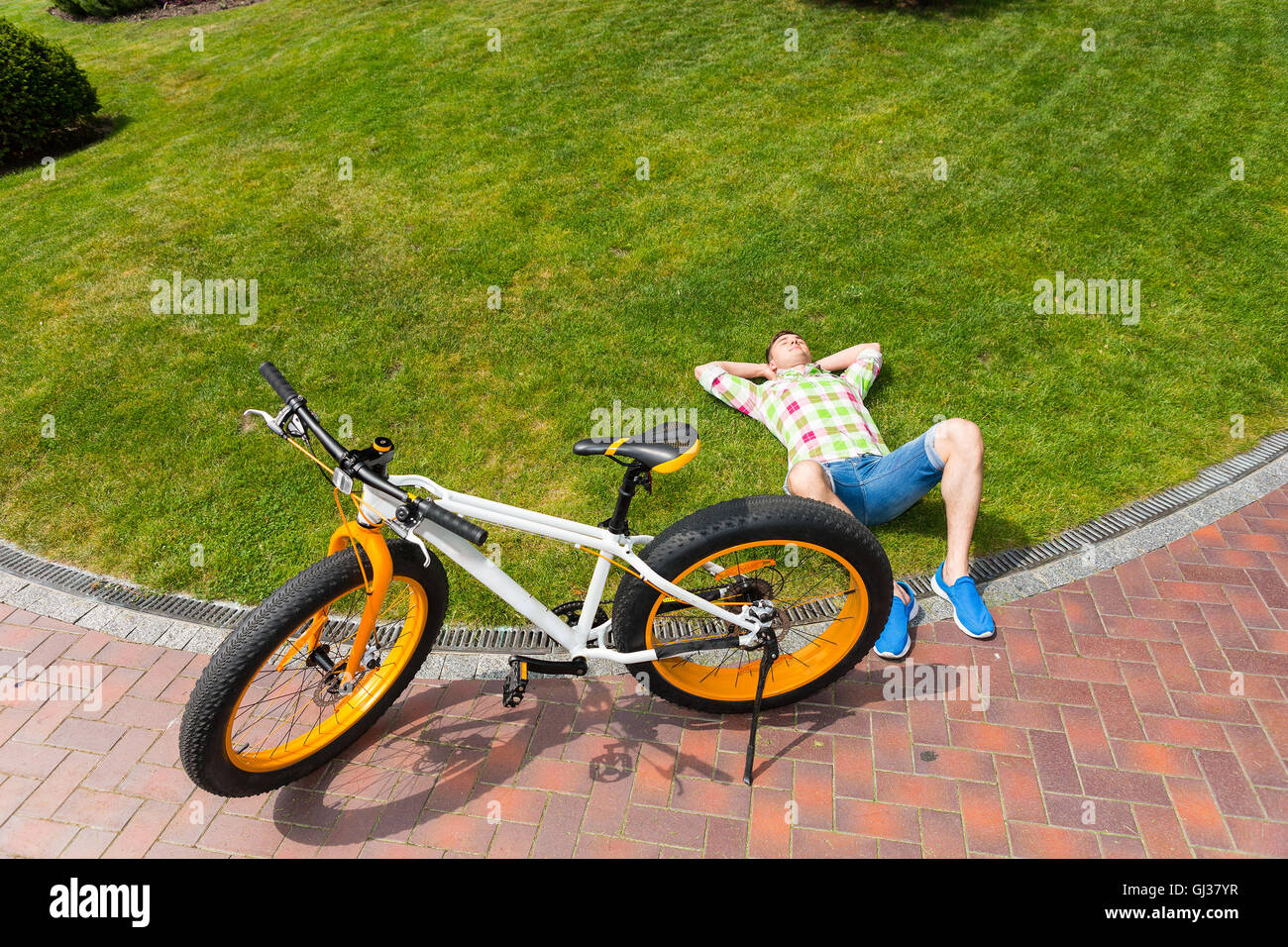 Top down view on relaxing man laying down on grass next to yellow and white  fat tire bicycle with copy space Stock Photo - Alamy