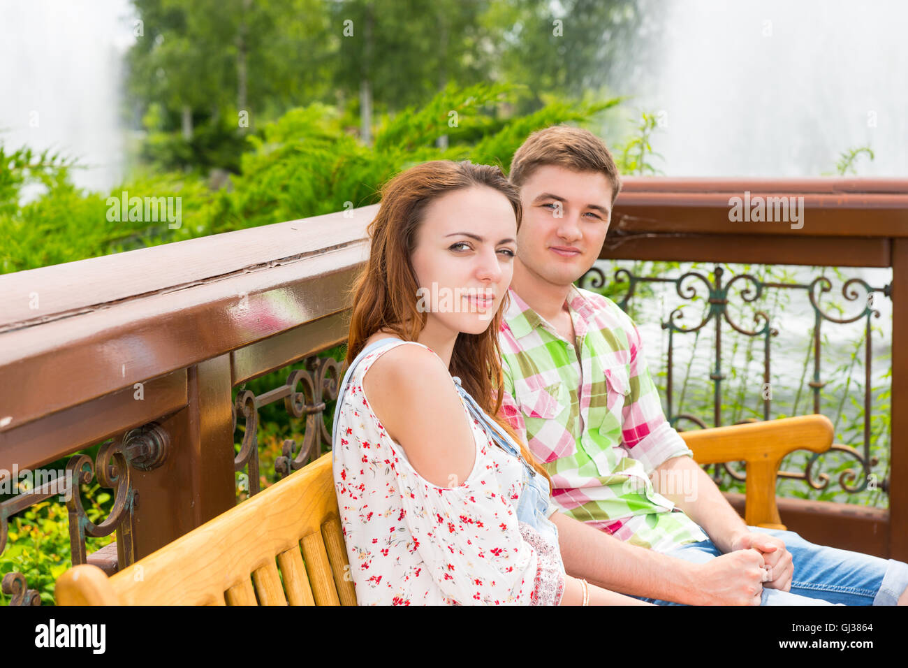 Young happy couple sitting on a bench in a park with fountain and ...