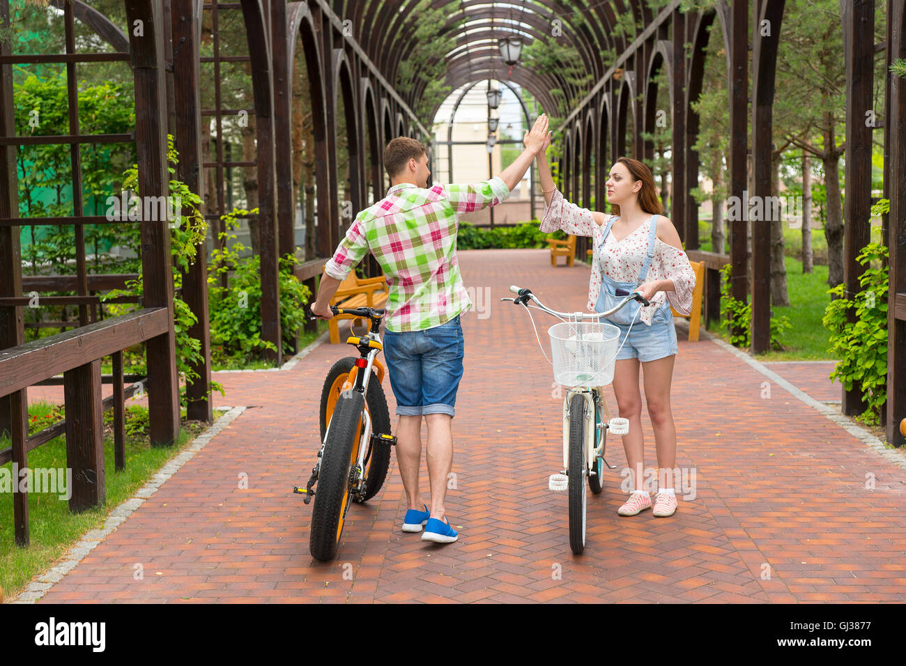 Happy young couple with bikes giving a high five each other in archway  in a park Stock Photo